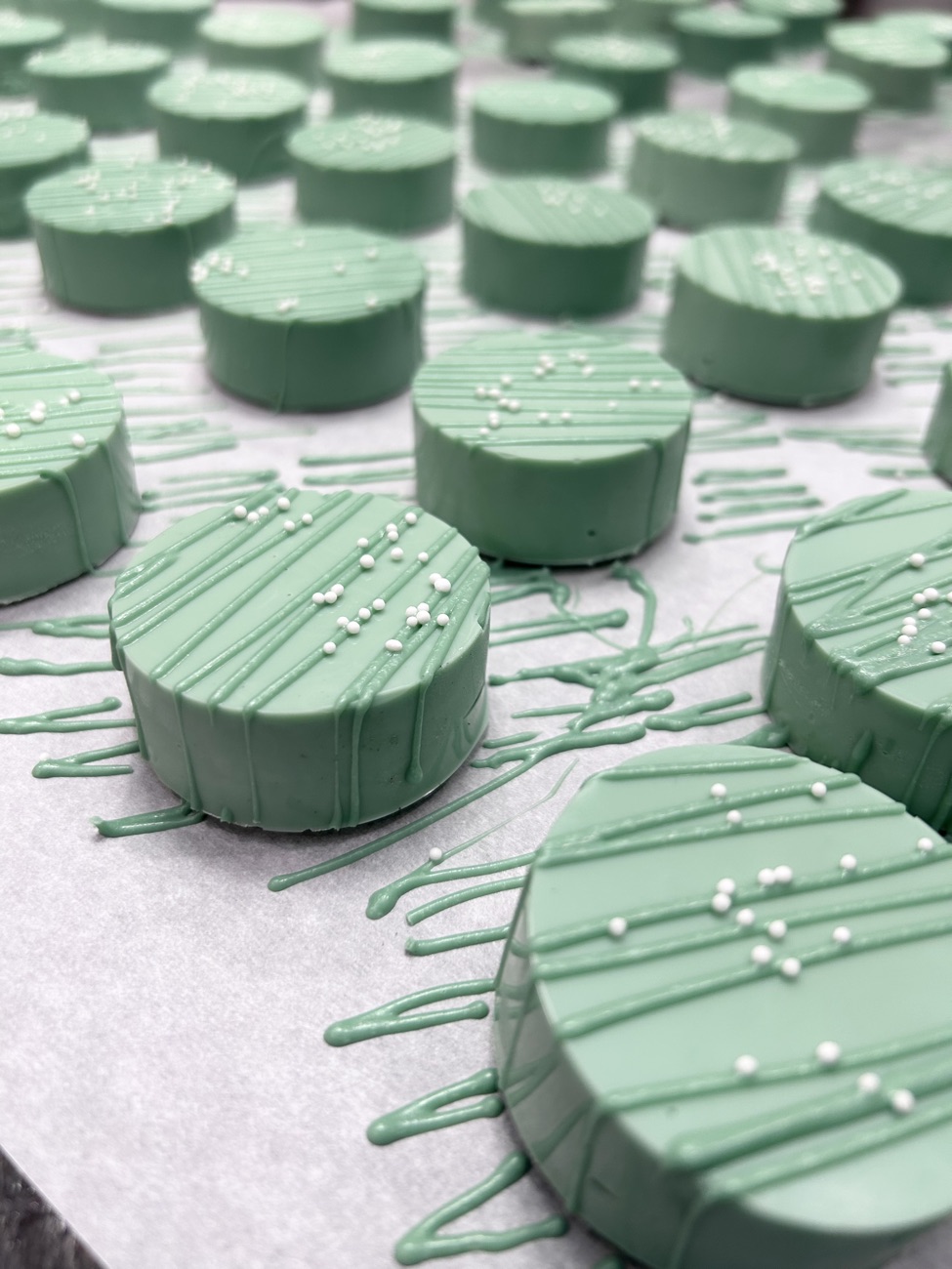 Sage green chocolate-covered Oreos with white nonpareils and drizzle