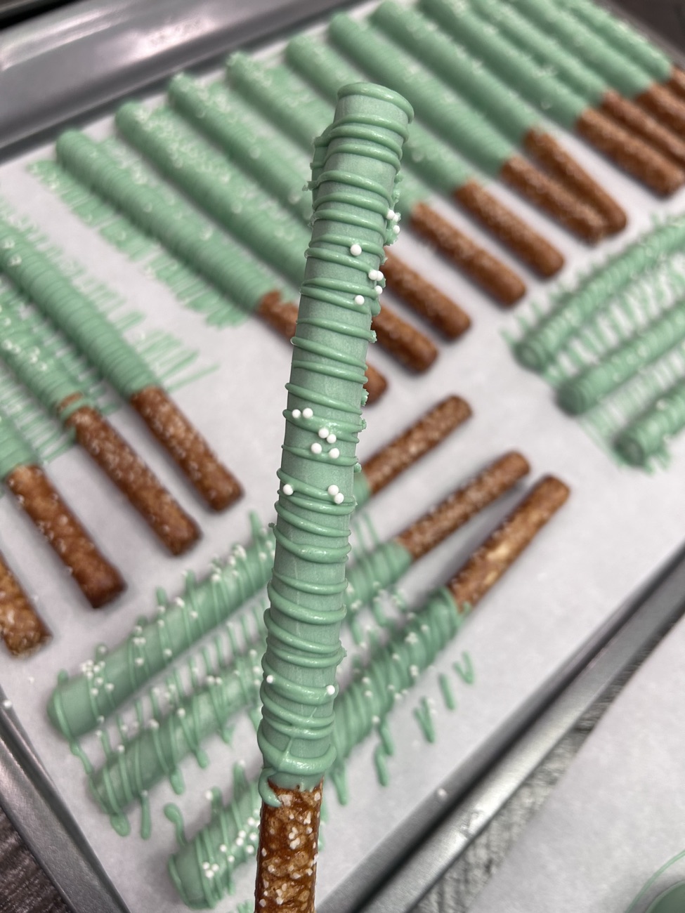 Sage green chocolate-dipped pretzel rods with white nonpareils and drizzle