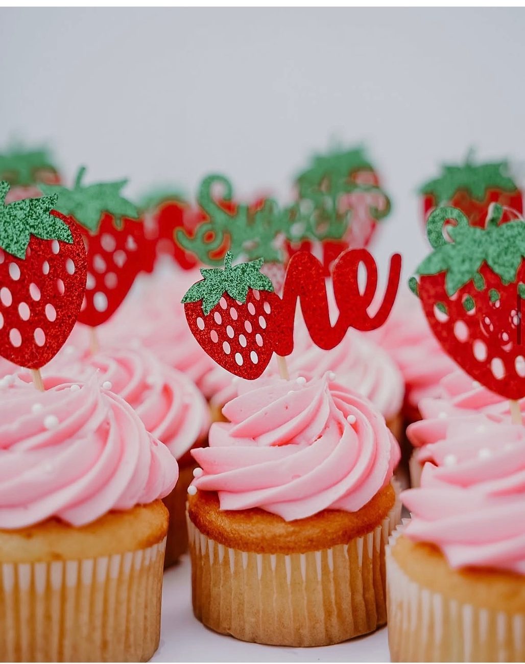 Pink-frosted cupcakes with strawberry and one toppers